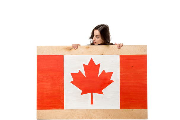 カナダ国旗に木の板の後ろに座って 白で隔離カメラ目線の女性 ロイヤリティフリー写真 画像素材