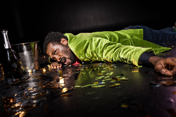 Selective focus of drunk african american man lying on floor with