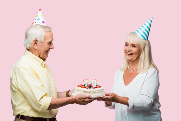 ピンクに隔離されたバースデーケーキを保持する灰色の髪を持つ肯定的なシニアカップル ロイヤリティフリー写真 画像素材