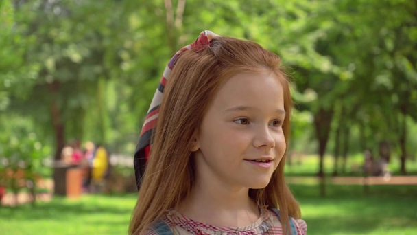 緑の日当たりの良い公園を歩くかわいい赤毛の子供 ストック動画映像