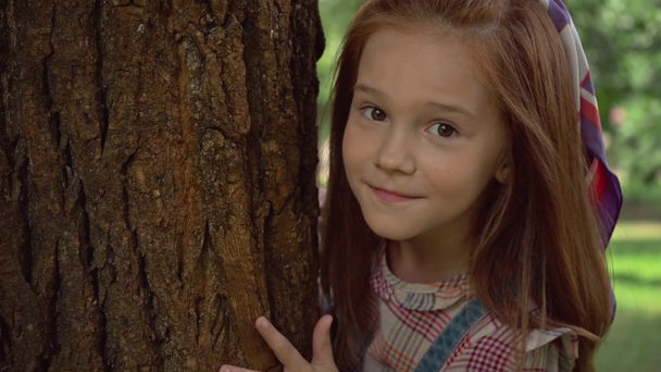 かわいい赤毛の子供が木の幹の後ろに隠れて舌を見せる ストック動画映像