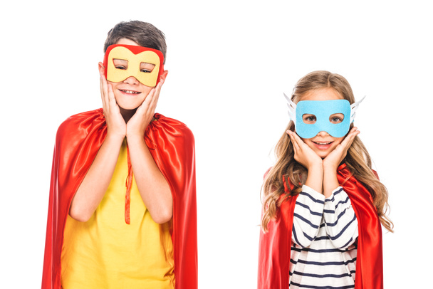 白で隔離されたマスクとヒーローマントの2人の笑顔の子供たちの正面図 ロイヤリティフリー写真 画像素材