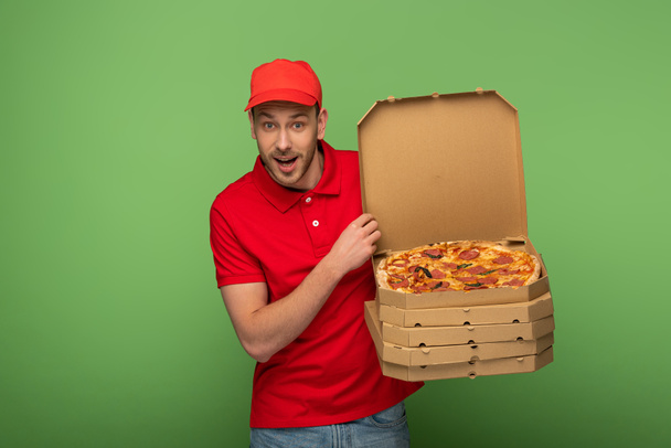 Excited delivery man in red uniform holding pizza boxes on green.