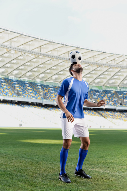 プロのサッカー選手がスタジアムでボールを頭にして青と白のユニフォームを着て ロイヤリティフリー写真 画像素材