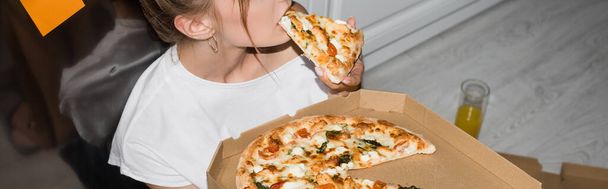 台所の床に座りながらピザを食べる若い女性のクロップドビュー パノラマショット ロイヤリティフリー写真 画像素材