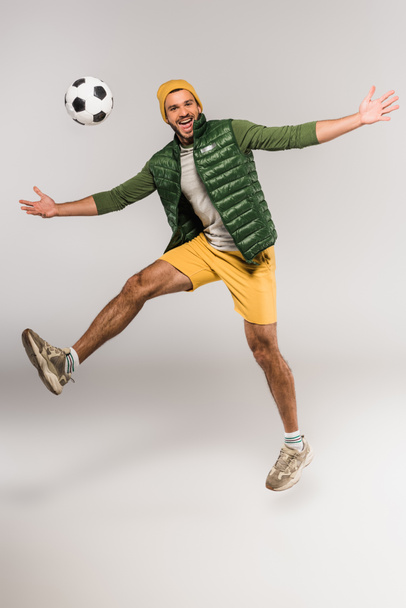 スポーツマンはグレーの背景に指でサッカーを保持しながらカメラで笑顔 ロイヤリティフリー写真 画像素材
