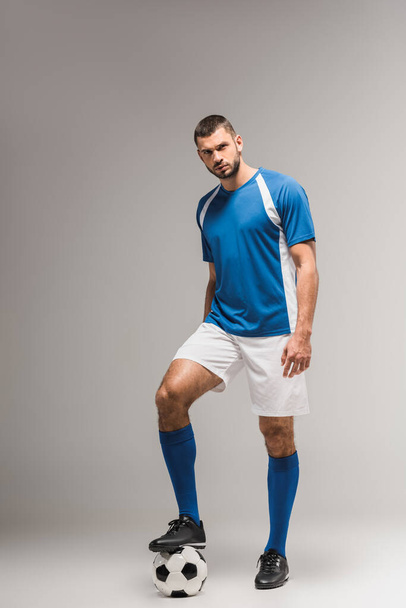 深刻なスポーツマンは灰色の背景にサッカーの横に立って ロイヤリティフリー写真 画像素材